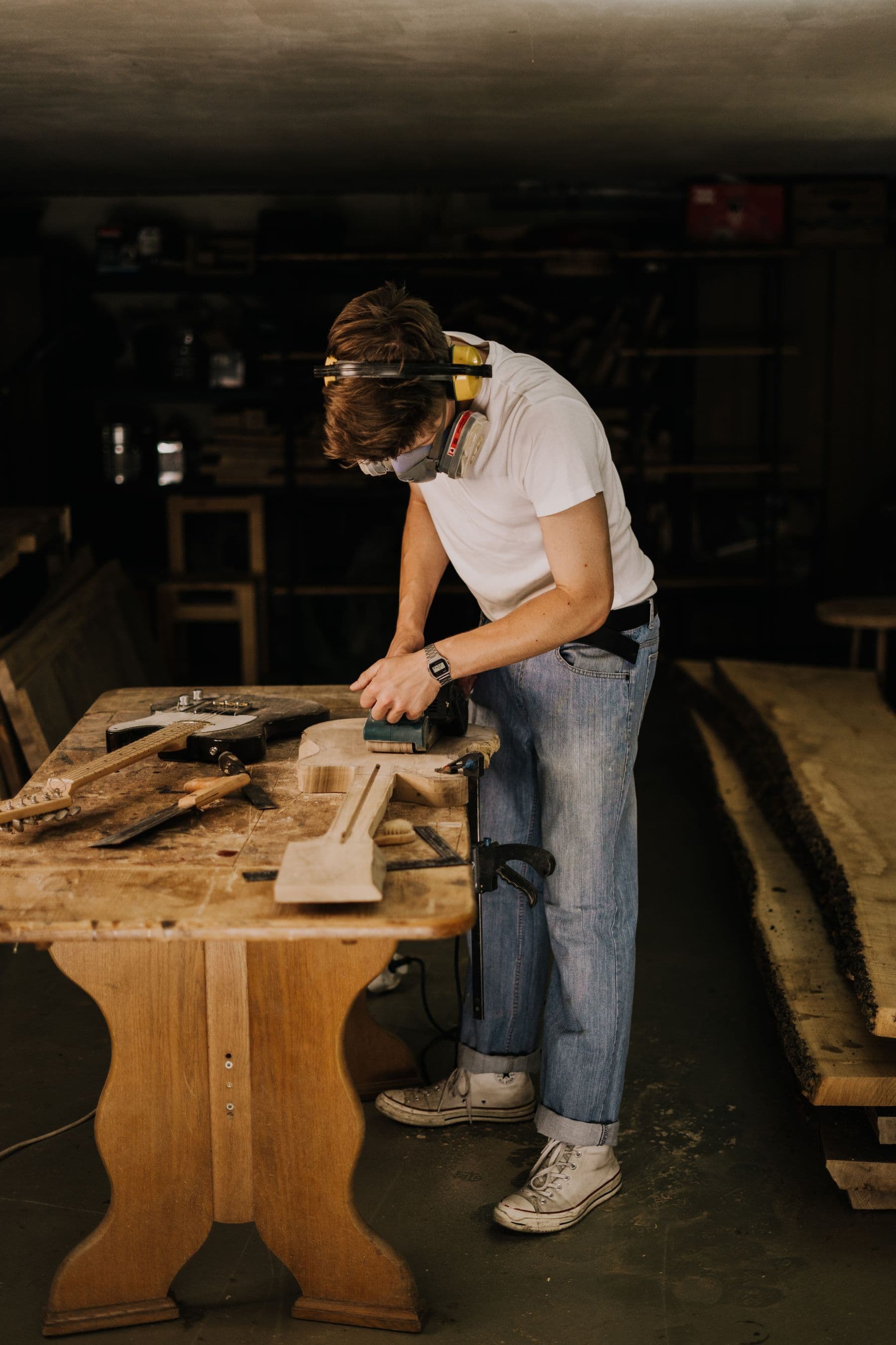 A craftsperson sanding a guitar body in a timber workshop
